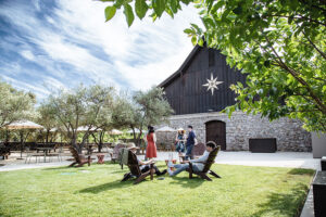 People sitting in large chairs on a green lawn with a barn with a star on it in the background